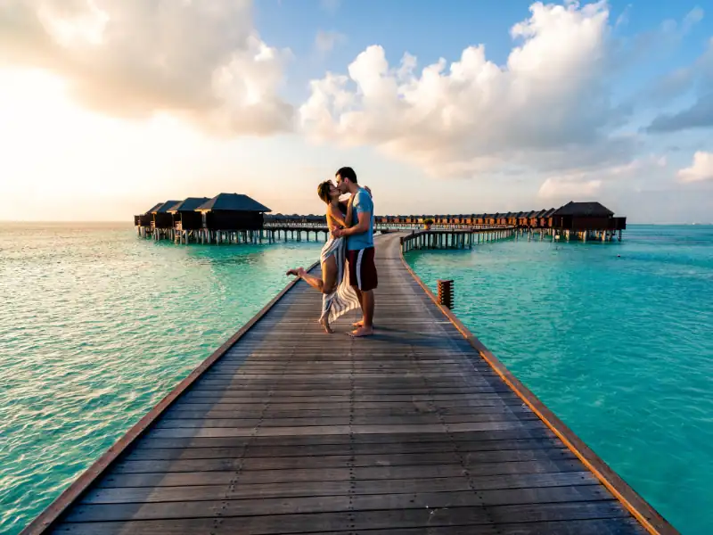 Couple romantique sur un ponton menant aux bungalows sur pilotis aux Maldives lors d'un voyage de noces.